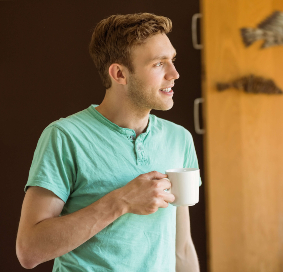 //precisionhairclinic.com/wp-content/uploads/2019/07/young-man-smiling-and-holding-coffee-at-home-in-PWDEW94-1.jpg
